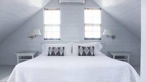 A bedroom with a large bed, two nightstands, two wall-mounted lamps, and two windows with curtains. - Charming Cottage in Harbour Island, minutes walk to Pink Sands beach (Dunmore Town)