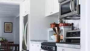A modern kitchen with stainless steel appliances, white cabinetry, and a wooden dining table in the background. - Charming Cottage in Harbour Island, minutes walk to Pink Sands beach (Dunmore Town)