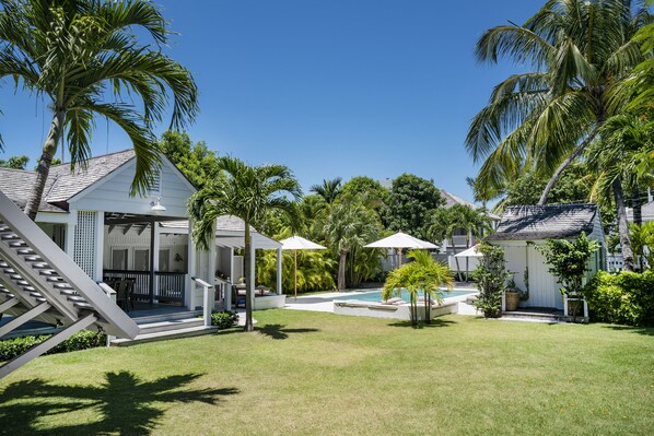 A backyard with a swimming pool, palm trees, and a covered patio area. - Charming Cottage in Harbour Island, minutes walk to Pink Sands beach (Dunmore Town)