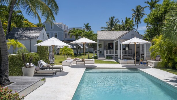 A pool area with lounge chairs and umbrellas, surrounded by palm trees and a house. - Charming Cottage in Harbour Island, minutes walk to Pink Sands beach (Dunmore Town)