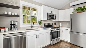 Una cocina moderna con armarios blancos, electrodomésticos de acero inoxidable, horno empotrado, microondas y lavavajillas.