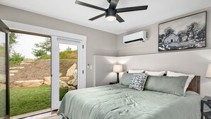 Un dormitorio con una cama, un ventilador de techo, una mesita de noche, una lámpara y un cuadro en la pared.