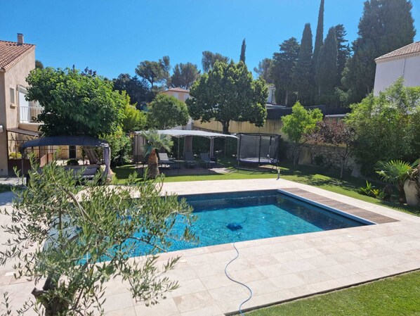 A rectangular swimming pool with a tiled deck, surrounded by a well-maintained lawn and various trees.