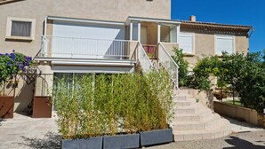 Een tweelaags huis met een balkon, een trap naar de bovenverdieping en een tuin met beplanting.