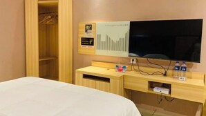 Quarto de hotel com cama, guarda-roupa de madeira, escrivaninha e uma pequena estante com televisão de tela plana.