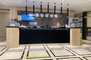 A hotel reception area with a black counter, multiple clocks, a digital screen, and a patterned floor. - Manjun Holiday Hotel (Nanning)