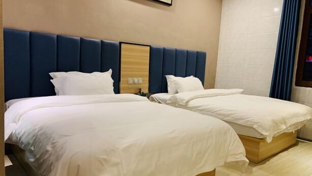 Quarto de hotel com duas camas, cabeceira azul e aparador de madeira.