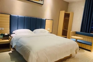 A hotel room with a large bed, a bedside table, a wardrobe, and a small round table.