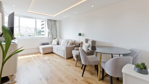 A modern living room with a sofa, chairs, a glass table, and a large window.