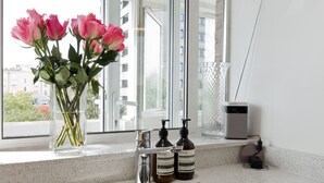 A bathroom with a sink, a glass vase with pink flowers, and two bottles of soap on the counter.