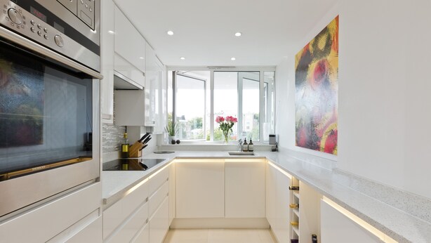 A modern kitchen with white cabinetry, a built-in oven, and a large window with a view of the city.