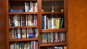 A bookshelf with various books and games, including a box of Scrabble and a box of Carmen Sandiego Junior Edition. - Charming Cupertino Retreat: Spacious Home near Apple HQ, Dining and Shopping! (Cupertino)