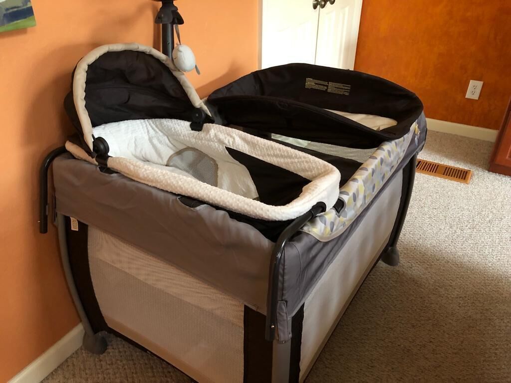 Ein Babywagen mit Moskitonetz und gepolstertem Sitz, platziert in einem Raum mit einer orangefarbenen Wand und einer weißen Tür.