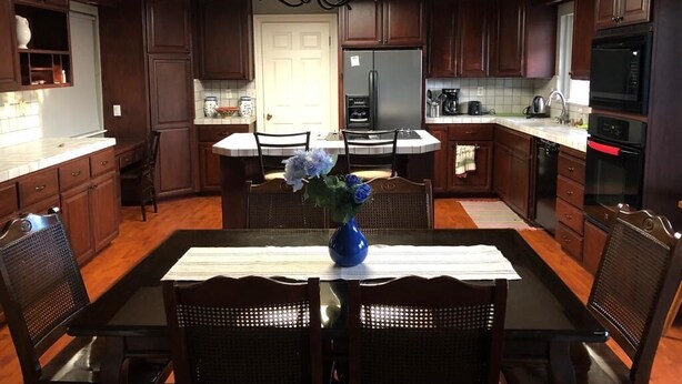 A modern kitchen with dark wood cabinets, a central island with seating, a chandelier, and a blue vase with flowers. - Charming Cupertino Retreat: Spacious Home near Apple HQ, Dining and Shopping! (Cupertino)