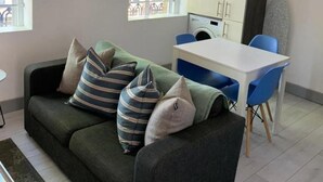 A modern living room with a dark green sofa, striped cushions, a white table, and blue chairs. - Beautiful 2-bed Apartment in Southend-on-sea (Southend-on-Sea)