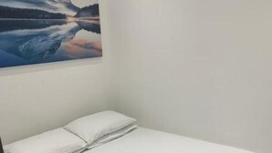 A single bed with white linens and pillows, a folded towel on the bed, and a painting of a mountain landscape on the wall. - Beautiful 2-bed Apartment in Southend-on-sea (Southend-on-Sea)