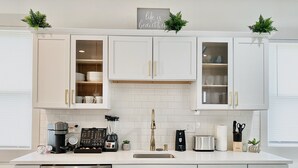 A modern kitchen with white cabinets, gold handles, and a central island with a coffee machine and toaster. - Hidden Gem in plain sight! Adorable 3 Bdrm Duplex near Hospitals & Universities. (Cincinnati)