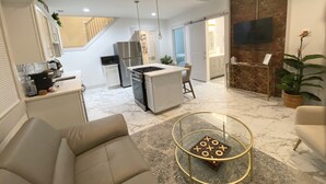 A modern living room with a sofa, a glass coffee table, and a kitchen area with a refrigerator, microwave, and stove. - Hidden Gem in plain sight! Adorable 3 Bdrm Duplex near Hospitals & Universities. (Cincinnati)