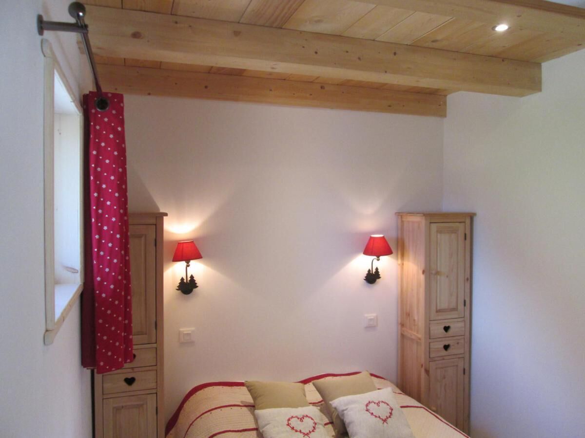 A bedroom with a wooden ceiling, a bed with heart-patterned pillows, two wall-mounted lamps, and a wardrobe.