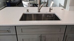 A kitchen with a stainless steel sink, a glass-top dining table, and grey cabinetry. - Lovely 2 bedroom luxury villa with a pool, Beach is 2 miles away. (Sarasota)