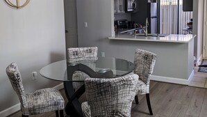 A dining area with a glass table and patterned chairs, a modern chandelier, and a view into the kitchen. - Lovely 2 bedroom luxury villa with a pool, Beach is 2 miles away. (Sarasota)