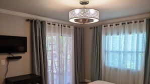 A bedroom with a bed, a TV mounted on the wall, and a ceiling light fixture. - Lovely 2 bedroom luxury villa with a pool, Beach is 2 miles away. (Sarasota)