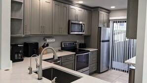 A modern kitchen with grey cabinets, stainless steel appliances, a built-in microwave, a refrigerator, and a sink with a faucet. - Lovely 2 bedroom luxury villa with a pool, Beach is 2 miles away. (Sarasota)