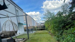 Een verzorgde achtertuin met een hangstoel, een trampoline en een klein tafeltje met speakers.