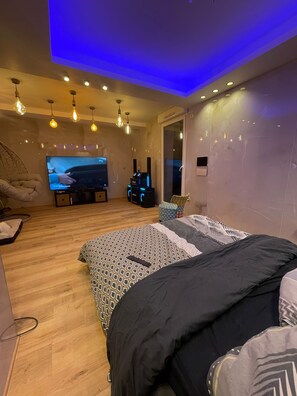 A modern bedroom with a large bed, a TV, and a gaming console. - Luxury suite with a private outdoor spa (Épinay-sur-Seine)