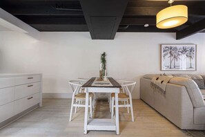 A dining area with a wooden table and white chairs, a sofa, and a framed picture on the wall. - Beachside 2-Bed House with Pool, Courtyard & BBQ (Sunshine Beach)