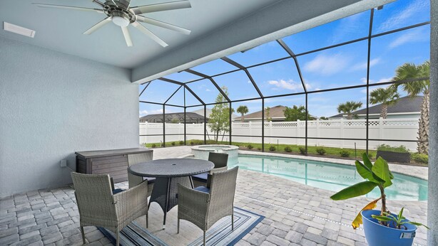 Eine Außenpatio mit Pool, Deckenventilator und Tisch mit Stühlen.