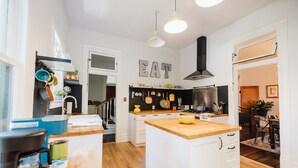 A modern kitchen with white cabinetry, wooden countertops, and a central island. There are hanging pots and pans, a coffee maker, and a visible stove. - Historical Houston - 2 king beds - vintage boho - centrally located (Houston)