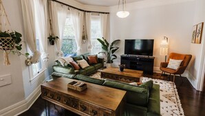 A living room with a green sofa set, a wooden coffee table, a TV, and a lamp. - Historical Houston - 2 king beds - vintage boho - centrally located (Houston)