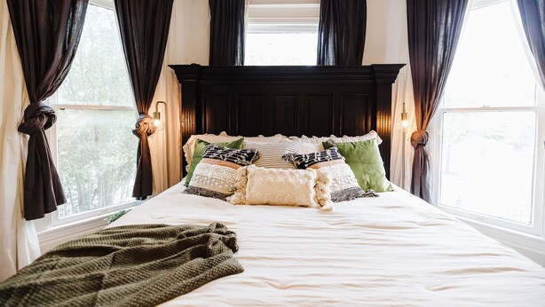 A neatly made bed with multiple pillows and a blanket, a dark wooden headboard, and a window with curtains. - Historical Houston - 2 king beds - vintage boho - centrally located (Houston)