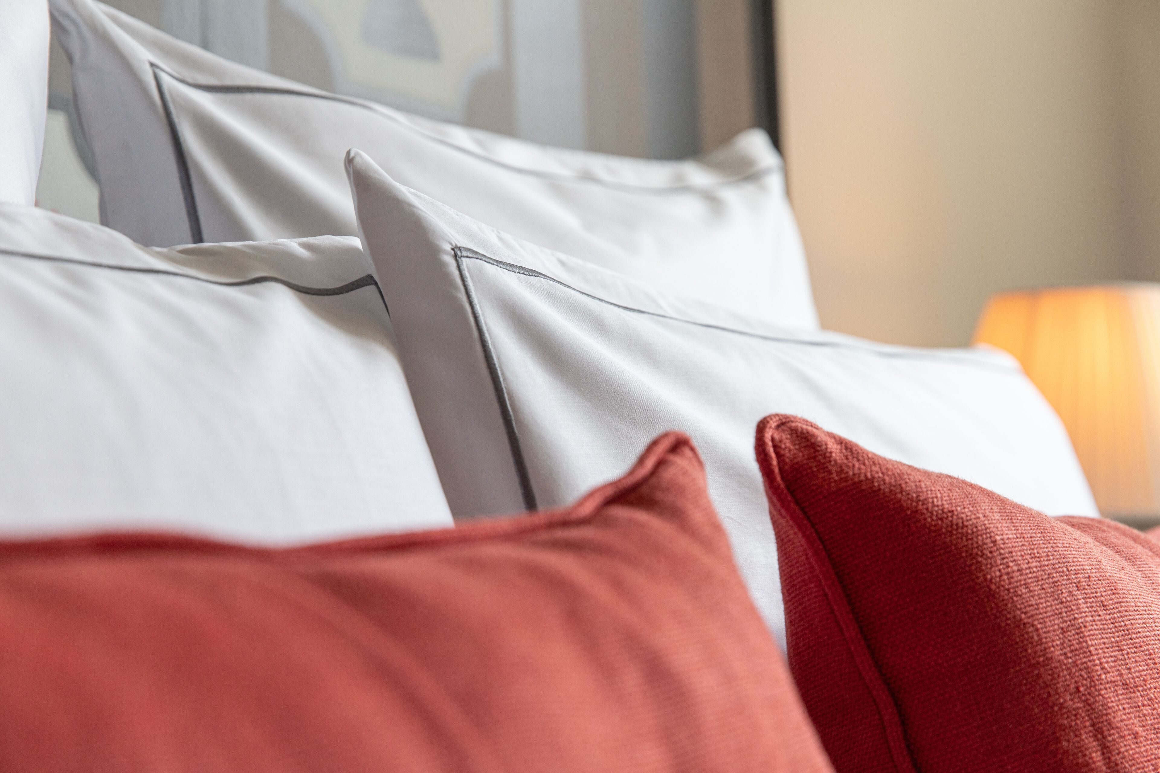 A bed with white and red pillows, a lamp in the background, and a striped wall.