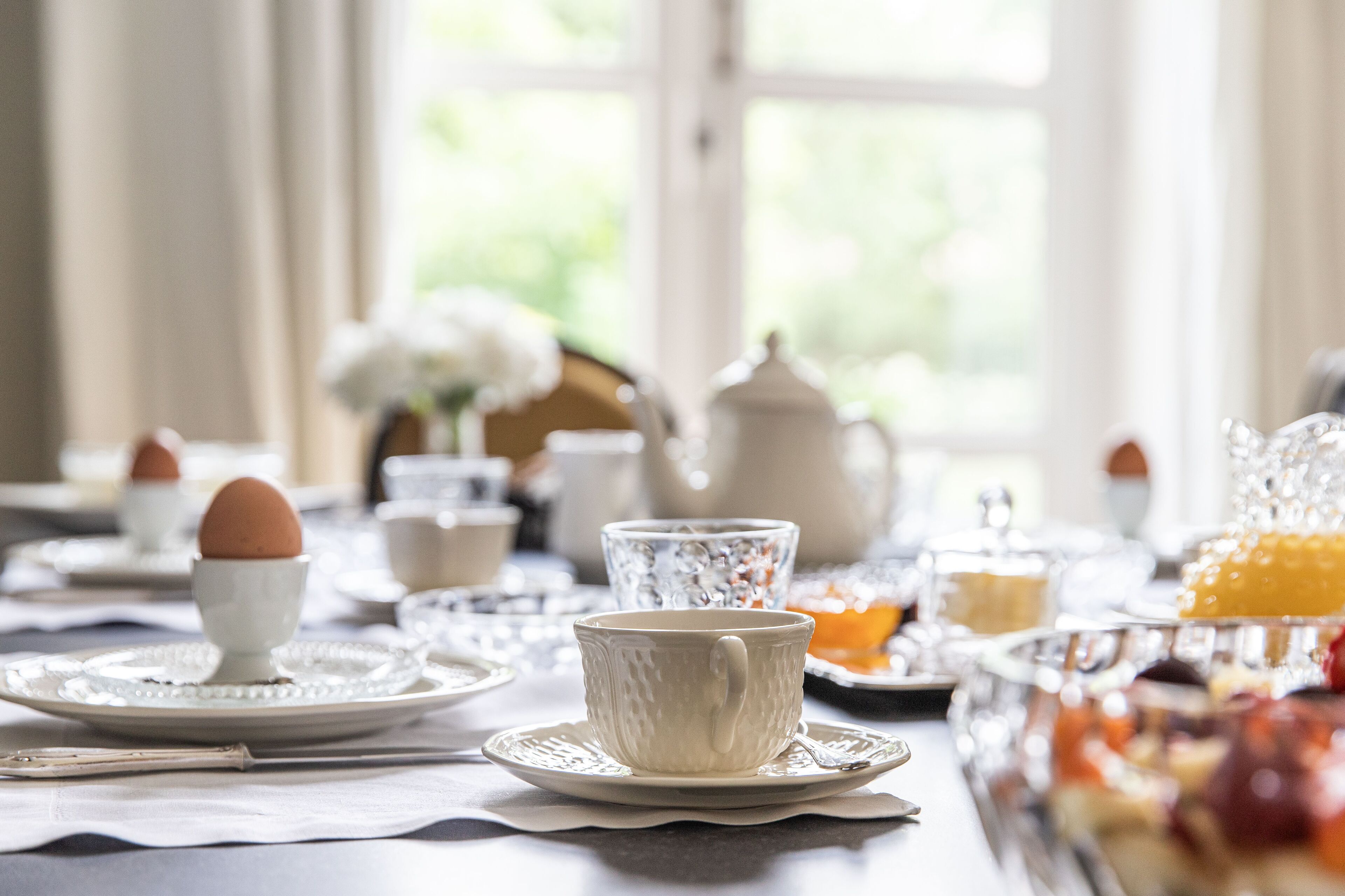 A breakfast setting with a table set for two, including plates, cups, and a teapot.
