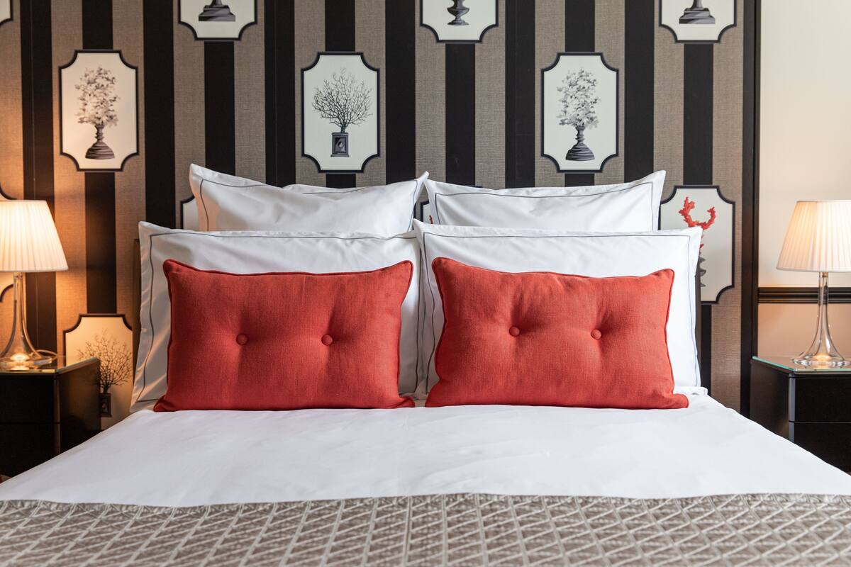 Un lit bien fait, avec des oreillers blancs et rouges, une couvre-lit à motifs et des œuvres d’art encadrées accrochées au mur.