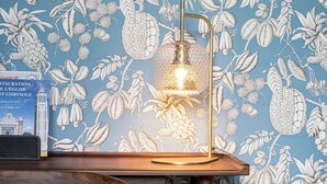 A room with a blue floral wallpaper, a wooden table with a lamp, and a framed picture on the wall. - La Castagnère de Bergory (Wervicq-Sud)