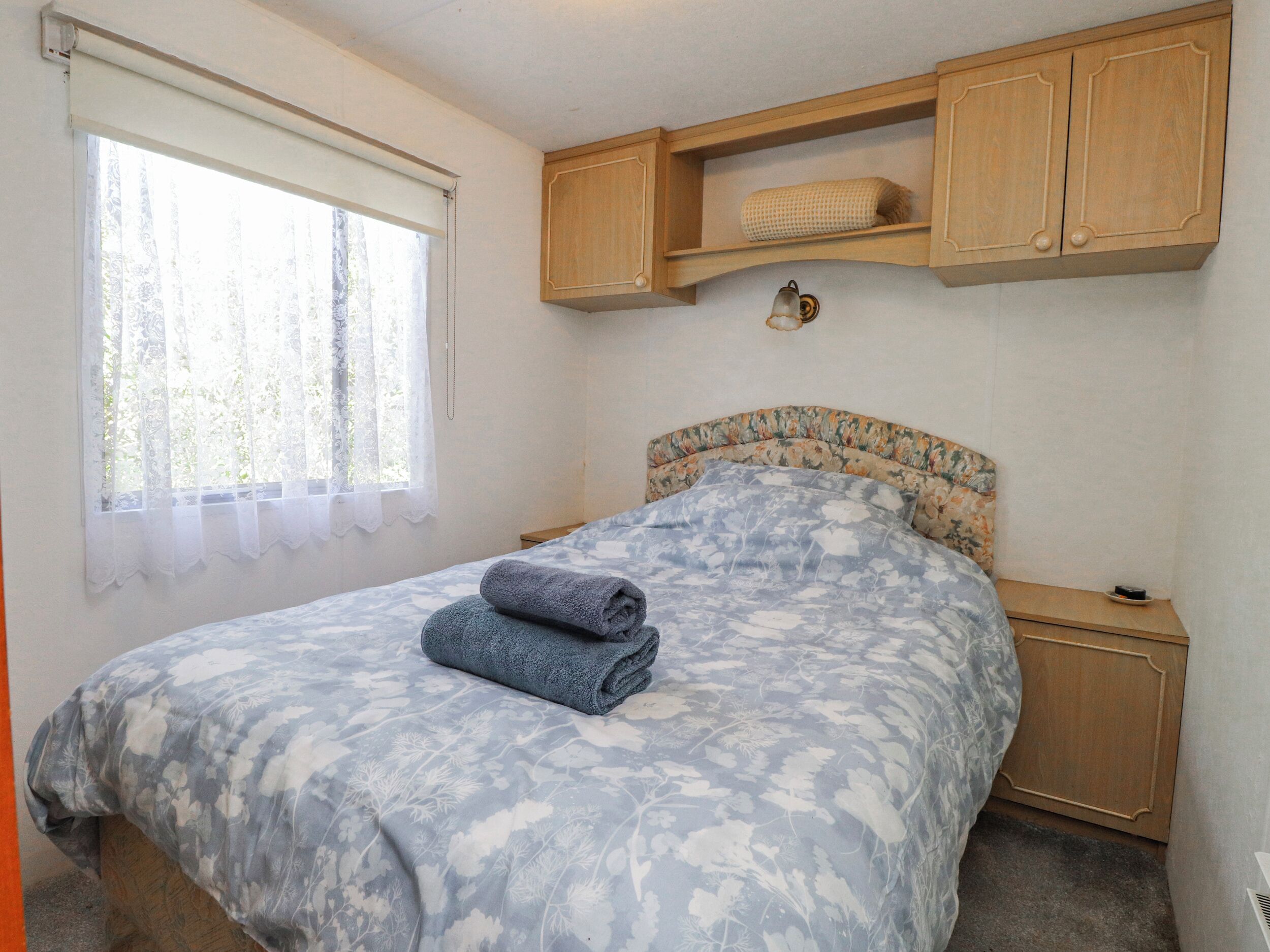 Un dormitorio con cama, ventana con cortinas, cabecero de madera y repisa sobre la cama.