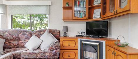 Un salón acogedor con un sofá estampado, un televisor de pantalla plana, armarios de madera y una chimenea.