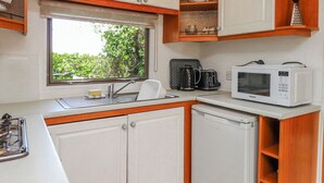 Una cocina compacta con armarios blancos, un ventanal con vistas a zonas verdes, un fregadero, un microondas y una cafetera.