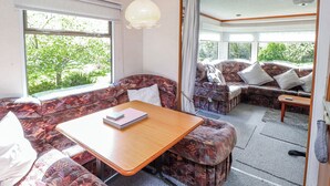 Interior acogedor de una caravana con sofá, mesa y vistas a la vegetación.