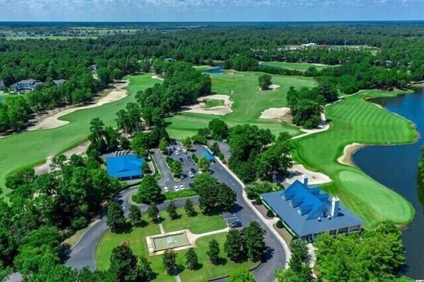 Vista aérea de um campo de golfe com um clube, parque de estacionamento e um lago.