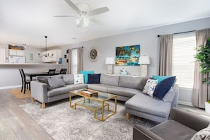 A modern living room with a sectional sofa, a glass coffee table, and a dining area with a chandelier.