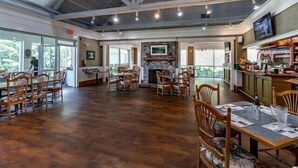 A spacious dining area with wooden flooring, multiple tables and chairs, a stone fireplace, and a television mounted on the wall. - Amazing 3BD 1st Floor Pawleys Island at True Blue Resort Golf 4 Pools Near Beach (Pawleys Island)