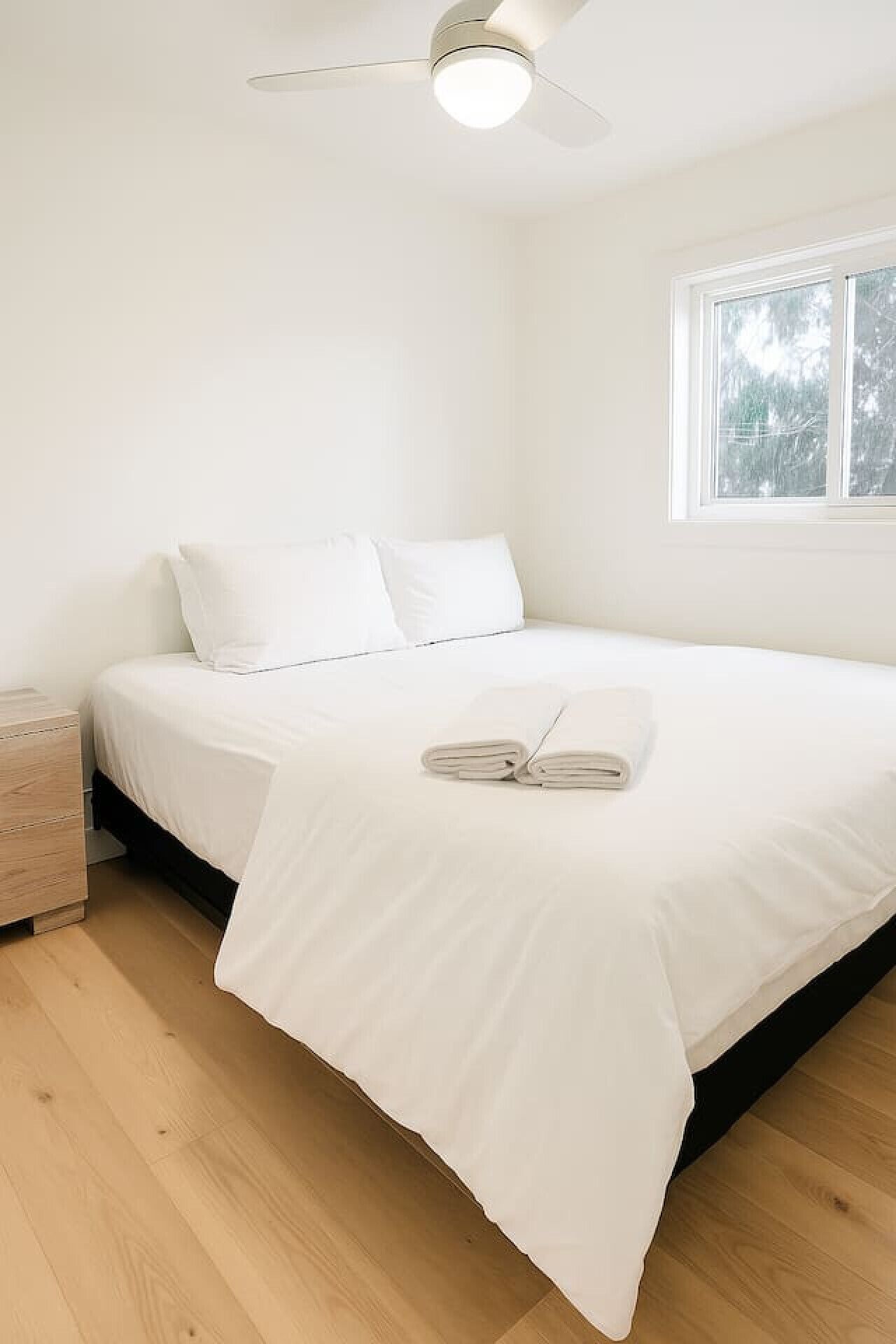 Une chambre à coucher avec un lit, une table de chevet, un ventilateur de plafond et une fenêtre.