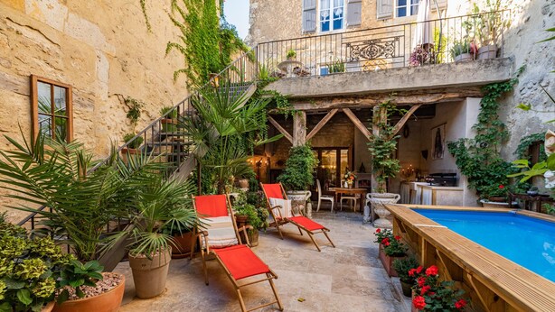 Un patio con piscina, mobiliario exterior y plantas en macetas.