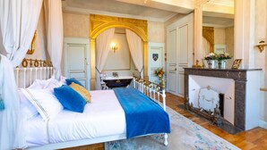 Un dormitorio lujoso con cama con dosel, un piano negro, chimenea y decoración elaborada.