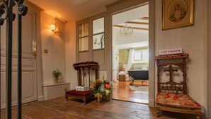 Un pasillo con piso de madera, un sillón antiguo, una mesita con cojín rojo y un cartel que dice "Taittinger".