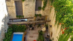 Un patio con piscina, plantas en macetas y una escalera que conduce a un balcón.